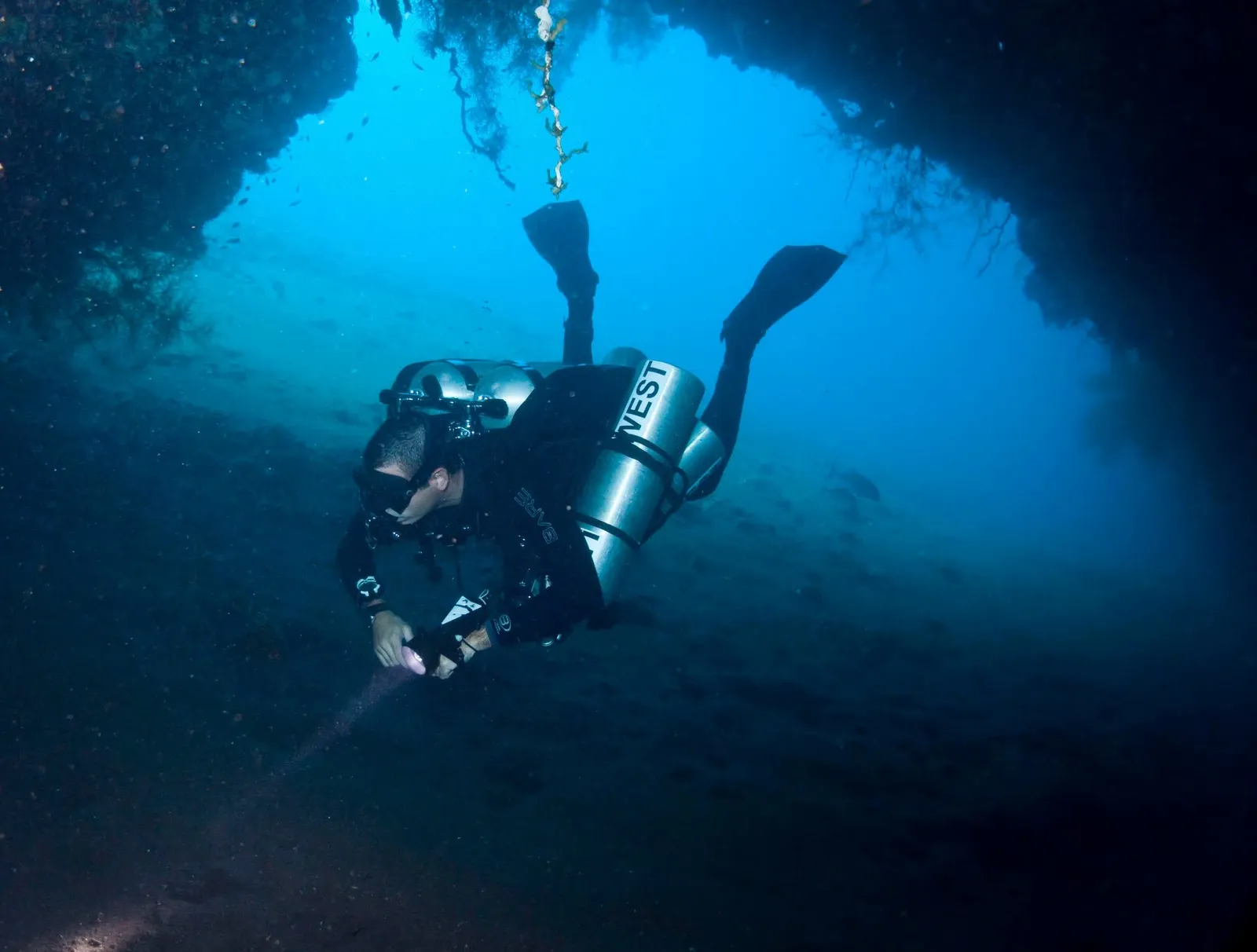 Tom West diving through an underwater cave with a light, twin tanks and a stage bottle
